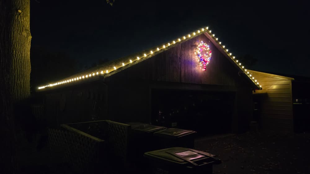 Detached garage roofline lit with warm white C9 bulbs and a wreath