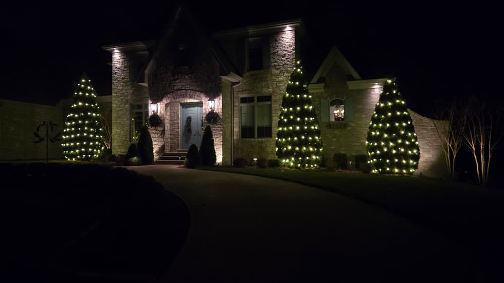 Stone home with landscape trees wrapped in warm white lights